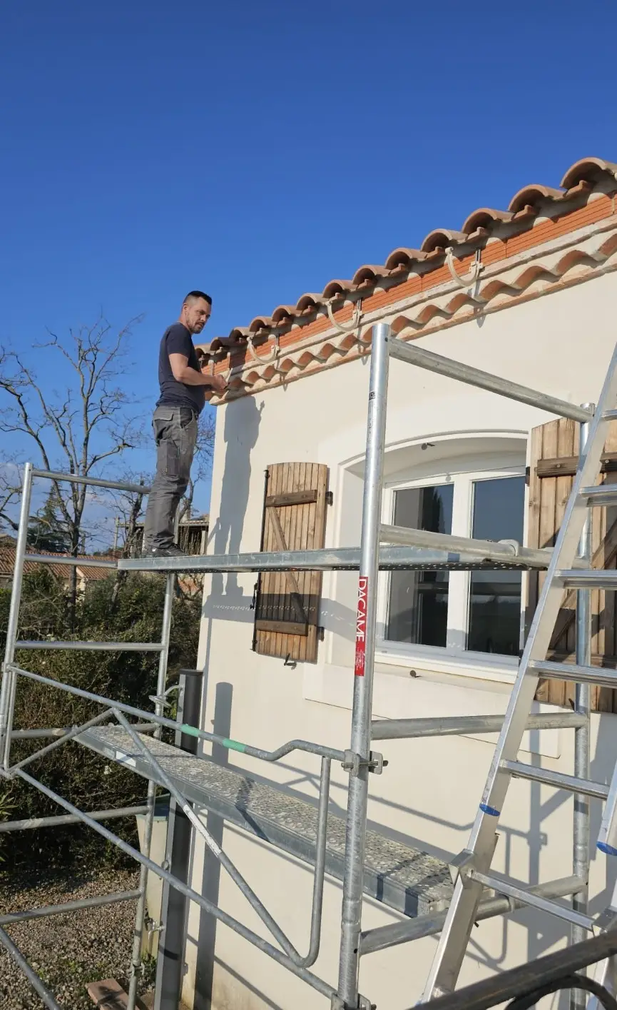 Le couvreur de MBS Roofing Work South France, debout sur un plateau d'échafaudage, installe des bandeaux de gouttières PVC en 33 en devant de toiture