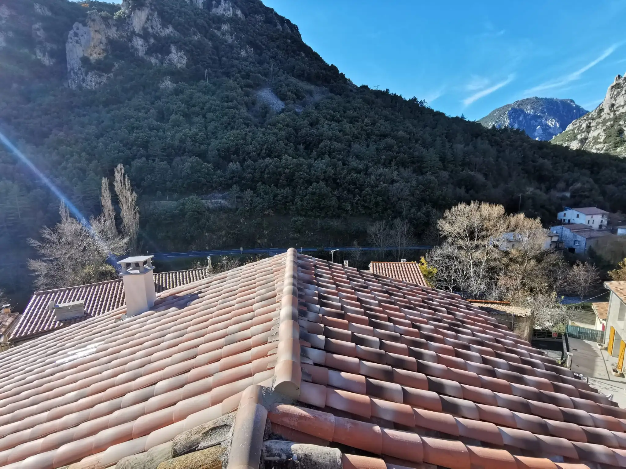 Faîtage neuf vu dans l'axe sur une toiture entièrement refaite, ciel dégagé et relief calcaire au fond