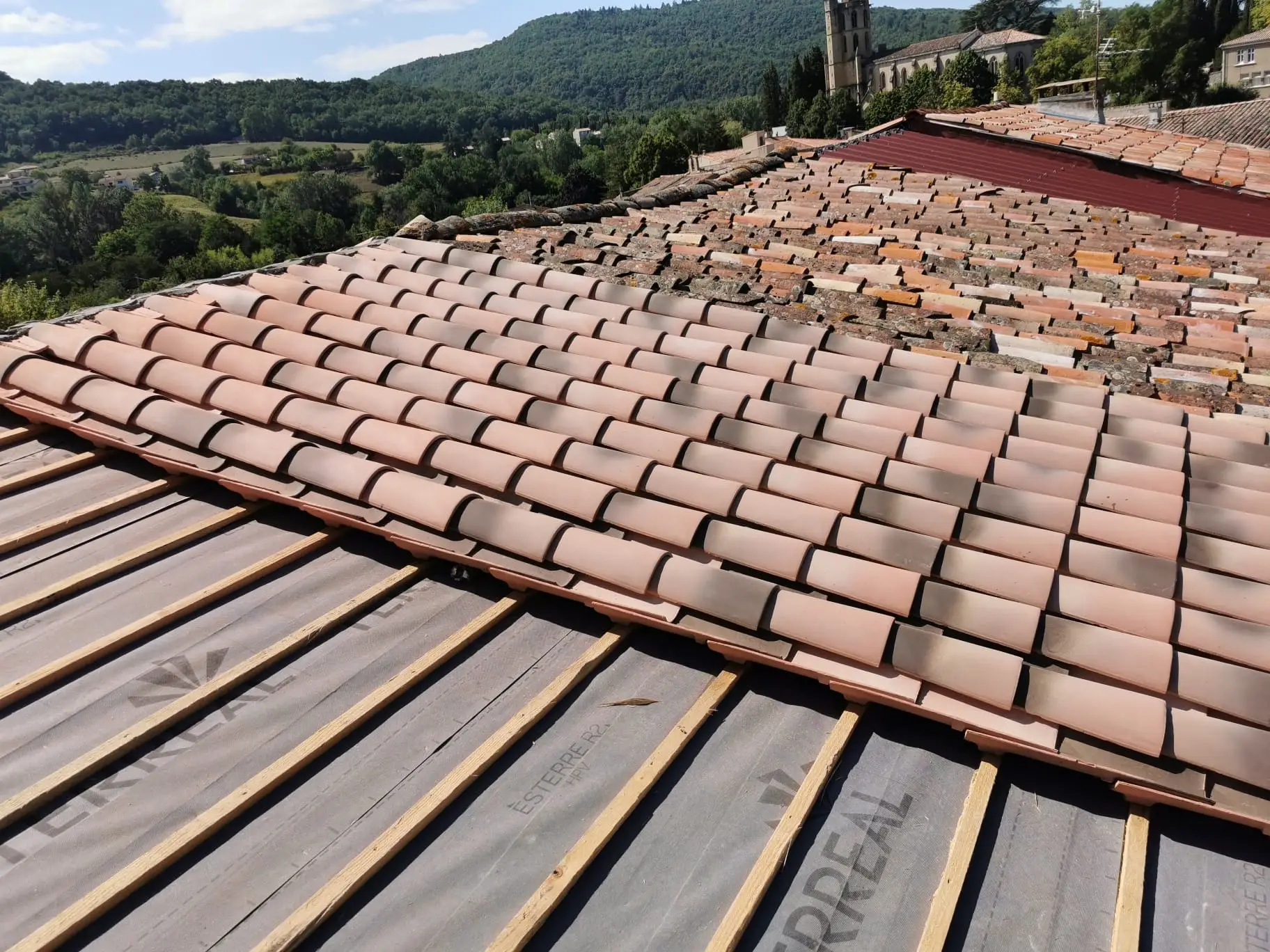 Progression d'une réfection de couverture : les tuiles canal reposées avancent rang par rang sur l'écran de sous-toiture neuf, l'ancienne couverture reste visible à droite