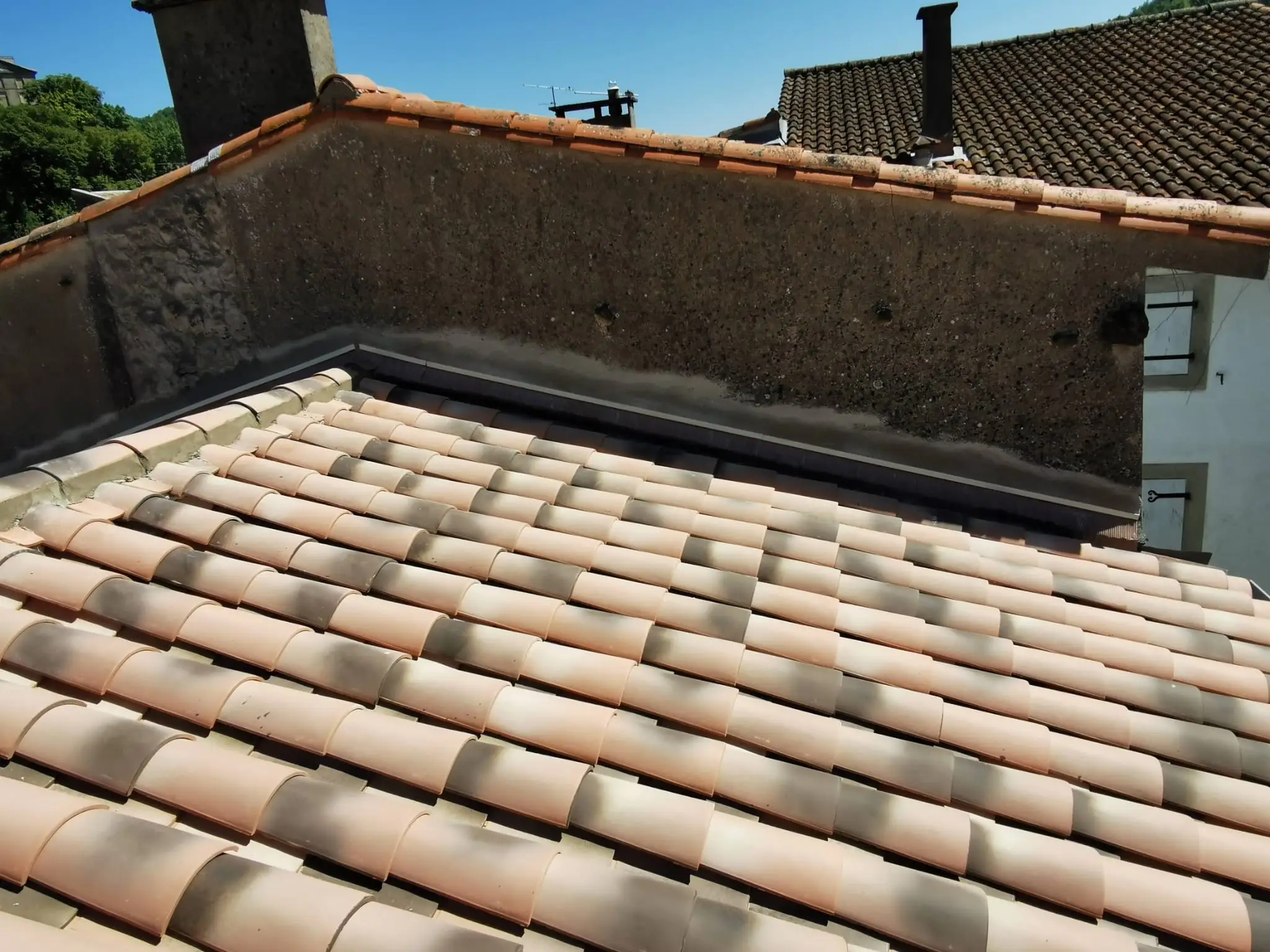 Couverture neuve en tuiles canal venant mourir contre un mur mitoyen ancien, avec une bande de zinc filant en pied de mur sur toute la longueur du raccord