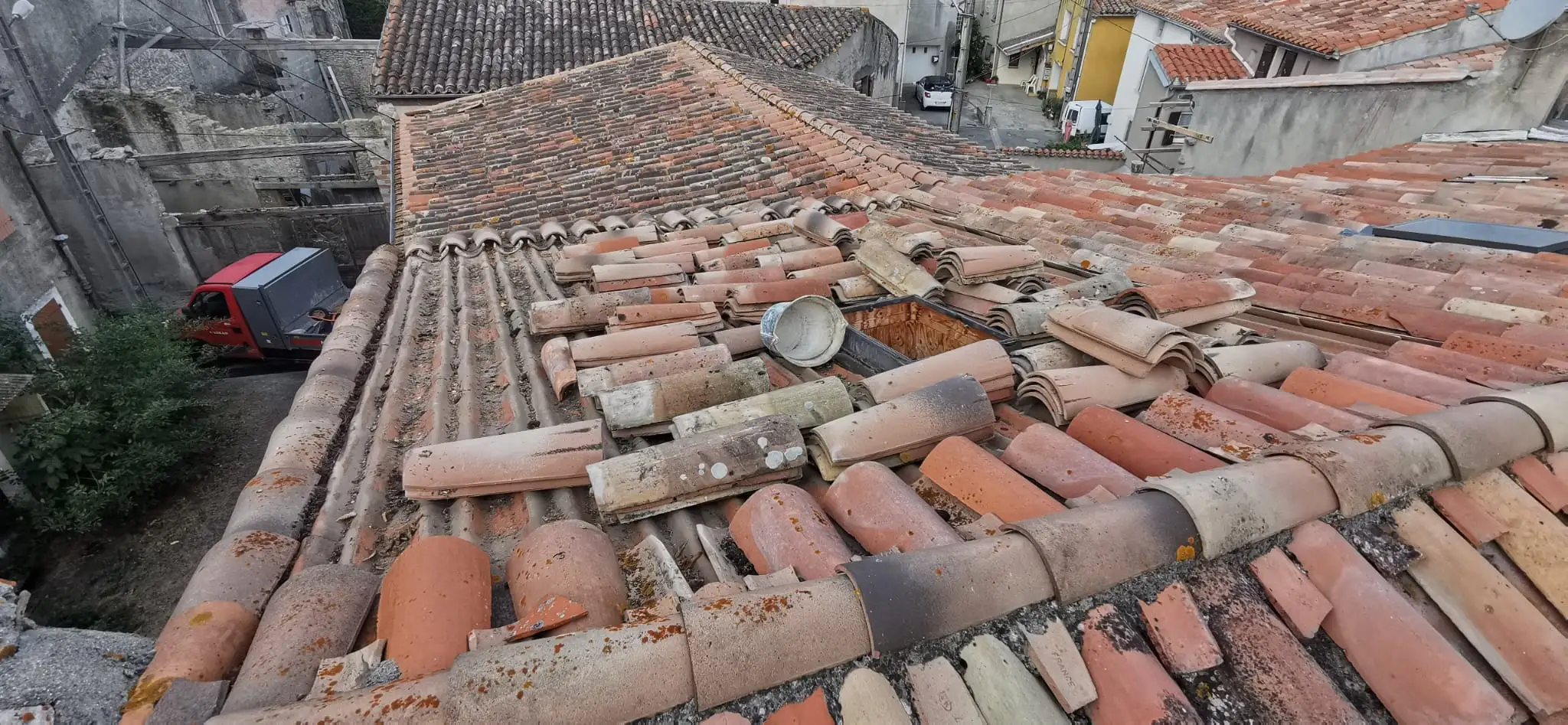 Couverture ancienne dégradée : tuiles cassées, déplacées et couvertes de mousse sur un pan entier de toiture