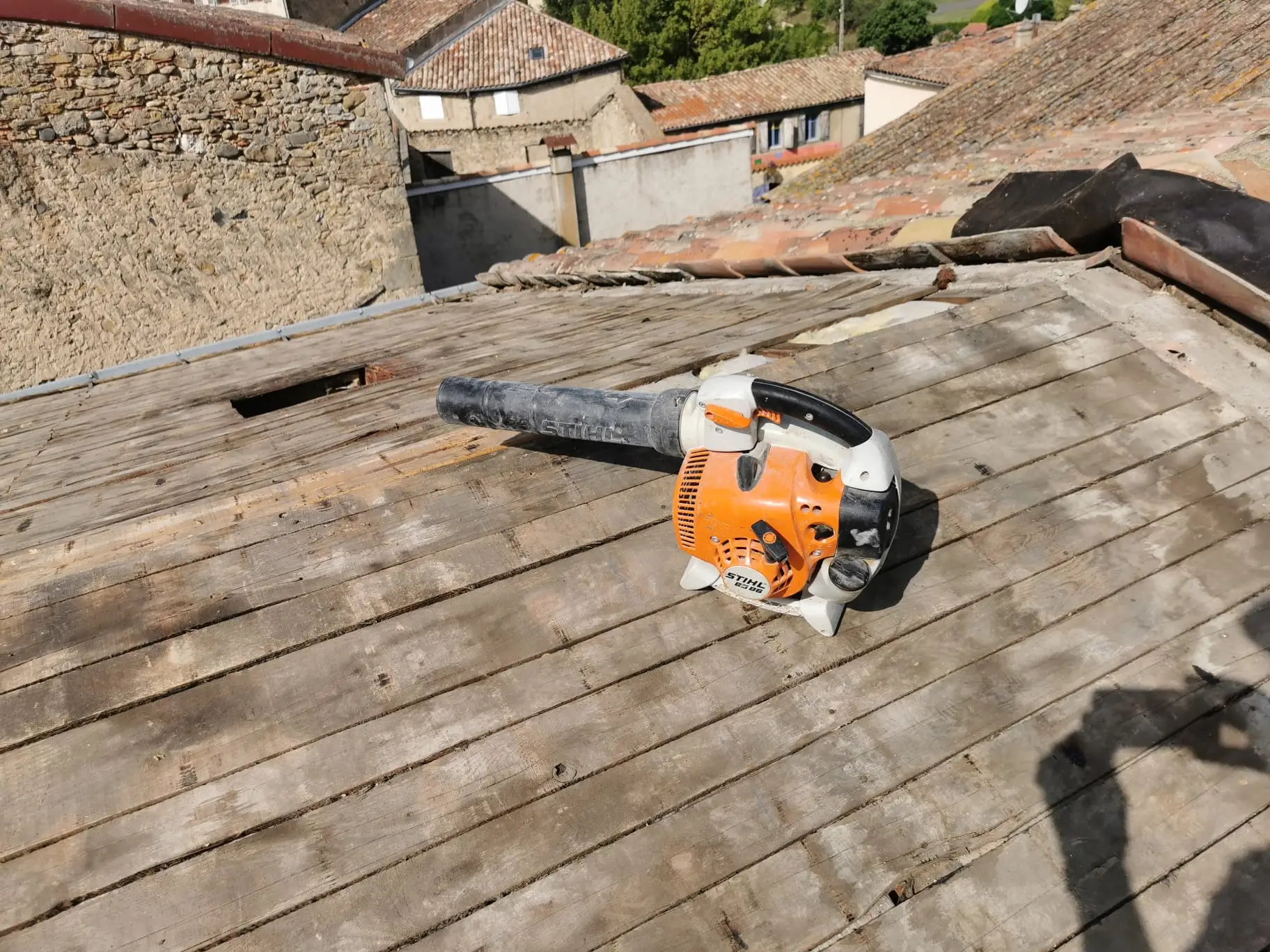 Rampant entièrement mis à nu : voligeage ancien apparent sur toute la surface, planches manquantes par endroits, toits et murs de pierre du village autour